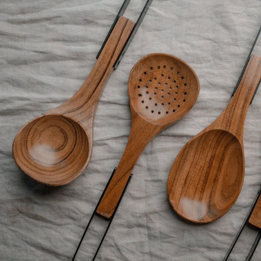 Set of Nordico kitchen utensils made of acacia wood with stainless steel handles laid out on a soft beige fabric.