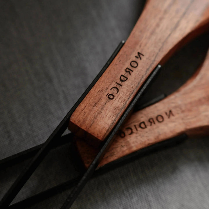 Detailed view of Nordico acacia wood kitchen utensils' handles engraved with the brand name, showing metal hanging hooks.