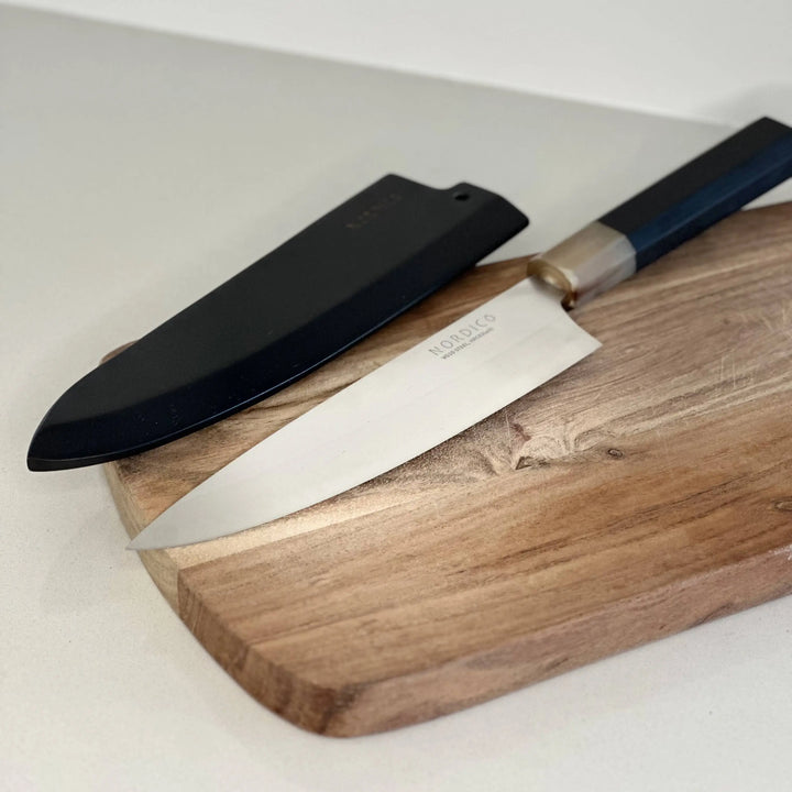 Nordico VG10 Chef Knife with black wooden sheath on a cutting board, showcasing its elegant design.