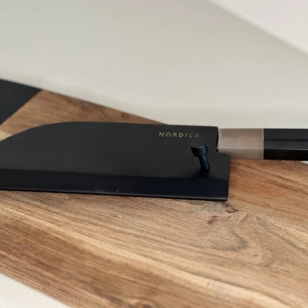 A Nordico VG10 cleaver knife with a sleek black wooden sheath resting elegantly on a wooden cutting board.