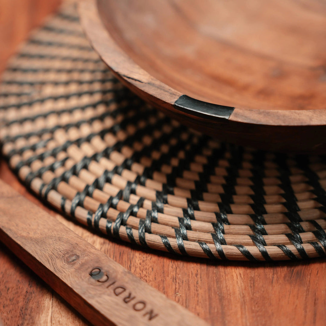 Close-up of NORDICO wooden bowl on a woven table mat, showcasing its unique handmade details and acacia wood texture.