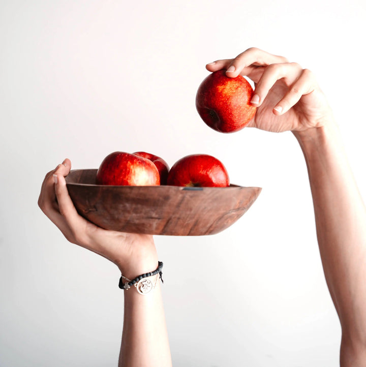 A person holding the NORDICO acacia wooden bowl filled with fresh red apples, showcasing its elegant and natural design.