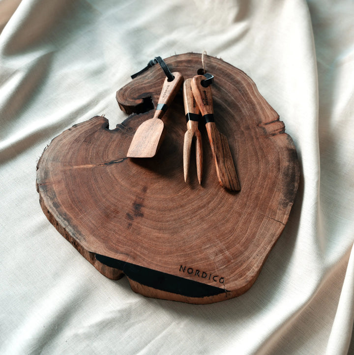 Nordico Cheese Board with Utensils (Stylized Shot) – Rustic acacia wood cheese board with cheese knives placed artfully, showcasing its irregular and unique natural shape.