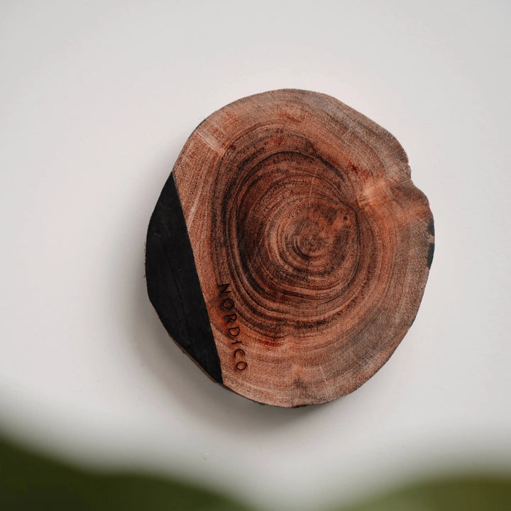 Single NORDICO Acacia wooden coaster with unique wood grain pattern and hand-painted black edge on a white background.