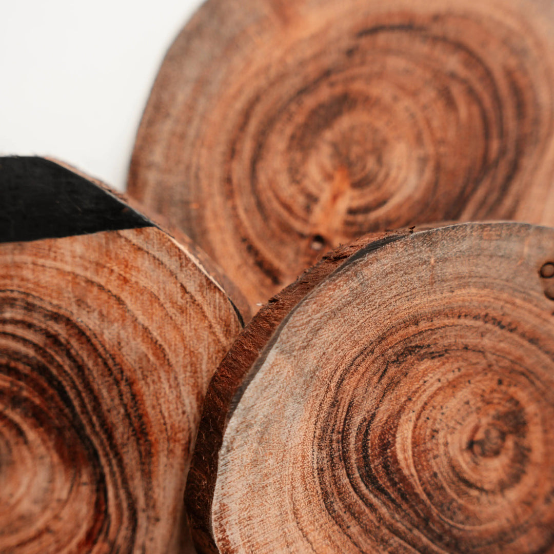 Set of three NORDICO Acacia wooden coasters showing unique grain patterns and hand-painted black accents on a white surface.