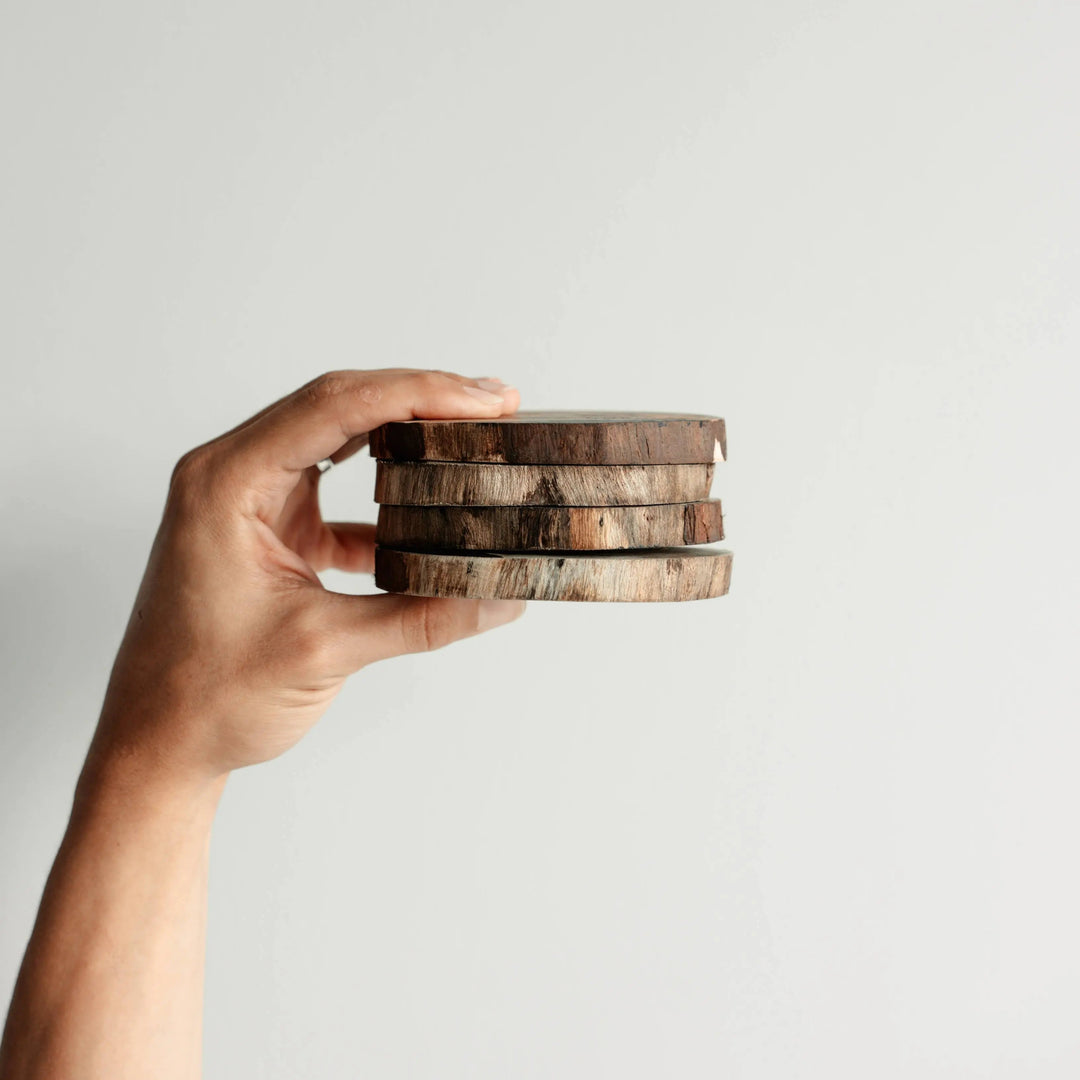 A hand holding a neatly stacked set of NORDICO Acacia wooden coasters, showcasing their smooth finish and rustic appearance.
