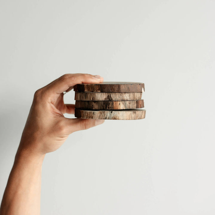 A hand holding a neatly stacked set of NORDICO Acacia wooden coasters, showcasing their smooth finish and rustic appearance.
