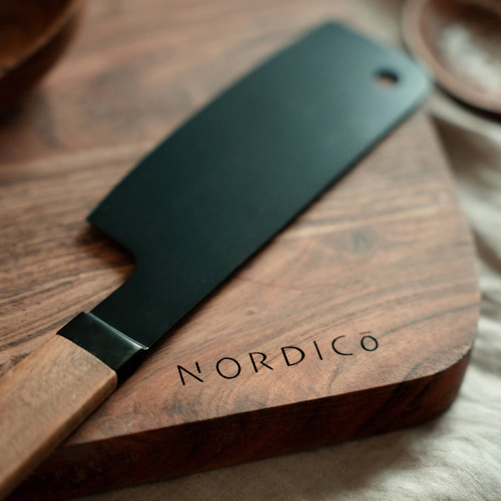 Close-up of a Nordico cutting board with a black knife resting on its smooth acacia wood surface.
