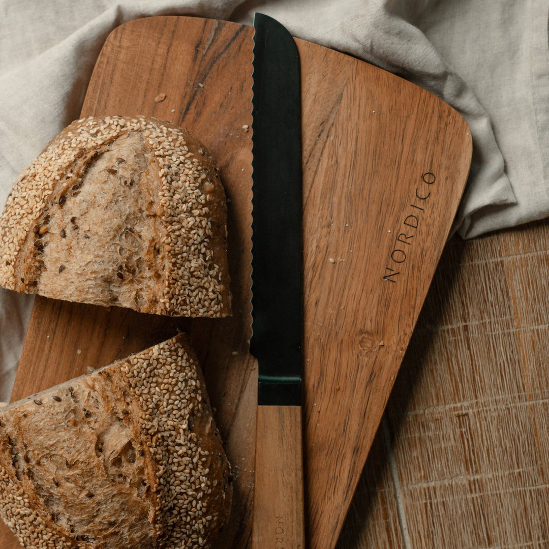 Nordico acacia cutting board with a black bread knife and sliced artisan bread, perfect for kitchen tasks and serving.
