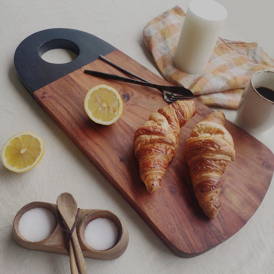 Nordico acacia wood cutting board styled with croissants, lemons, and coffee for a breakfast setting.