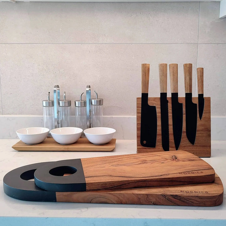 Modern kitchen display featuring Nordico acacia cutting boards with black-painted handles and a matching knife block set.