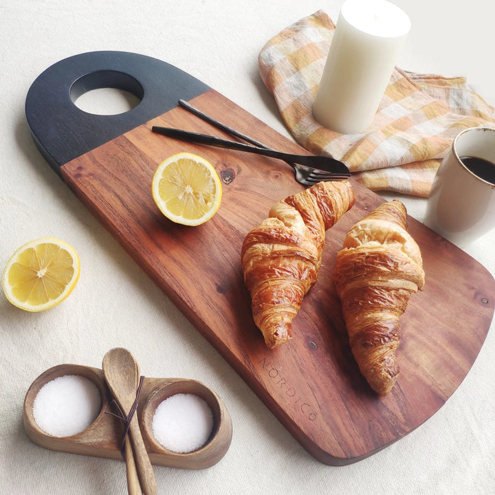 Nordico acacia wood cutting board styled with croissants, lemons, and coffee for a breakfast setting.