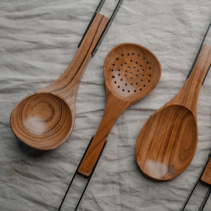 Set of Nordico kitchen utensils made of acacia wood with stainless steel handles laid out on a soft beige fabric.