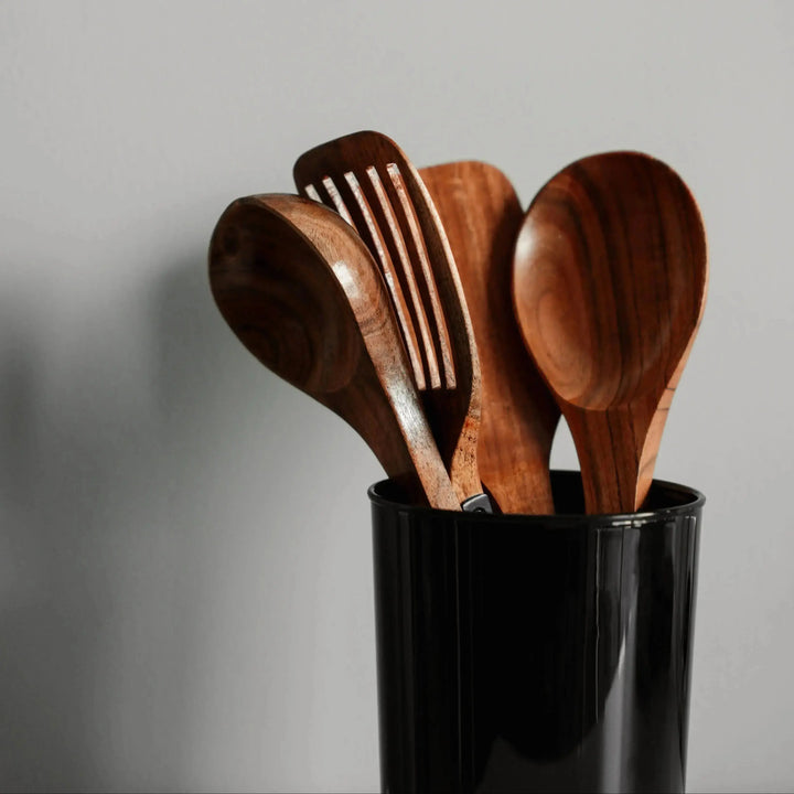 Nordico acacia wooden kitchen utensils displayed in a black holder against a neutral wall background.