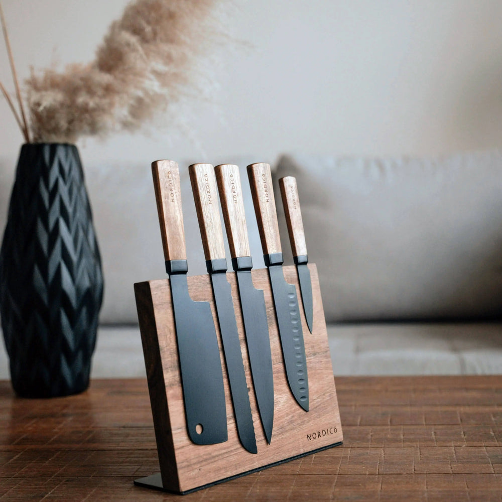 Luxury Nordico 5-piece stainless steel kitchen knives set with acacia handles on a modern wooden table.