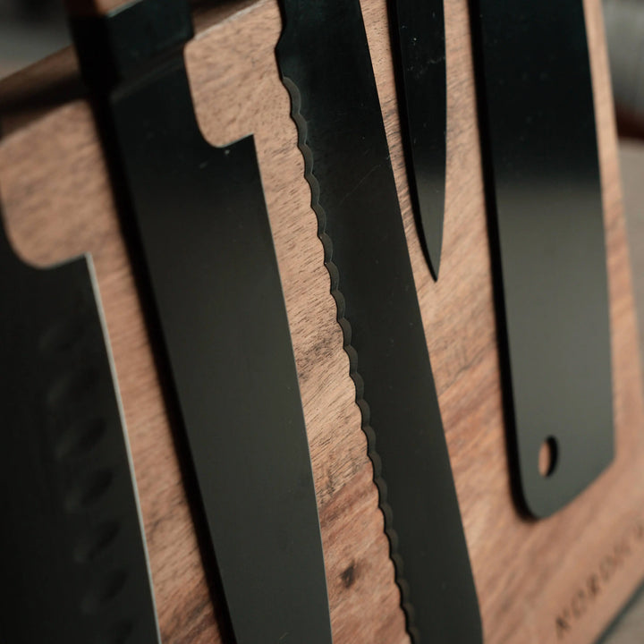 Close-up of Nordico stainless steel kitchen knives with black blades and acacia wood handles.