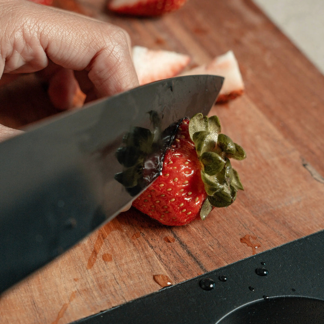 Nordico stainless steel knife in use, slicing a fresh strawberry on a wooden cutting board.