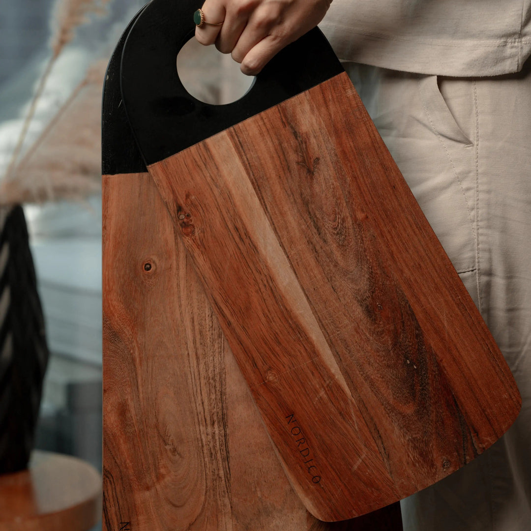 Person holding Nordico medium and large acacia cutting boards, displaying their ergonomic black handles.