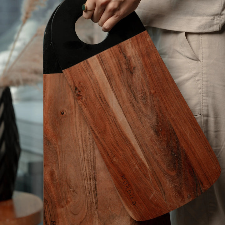 Person holding Nordico medium and large acacia cutting boards, displaying their ergonomic black handles.