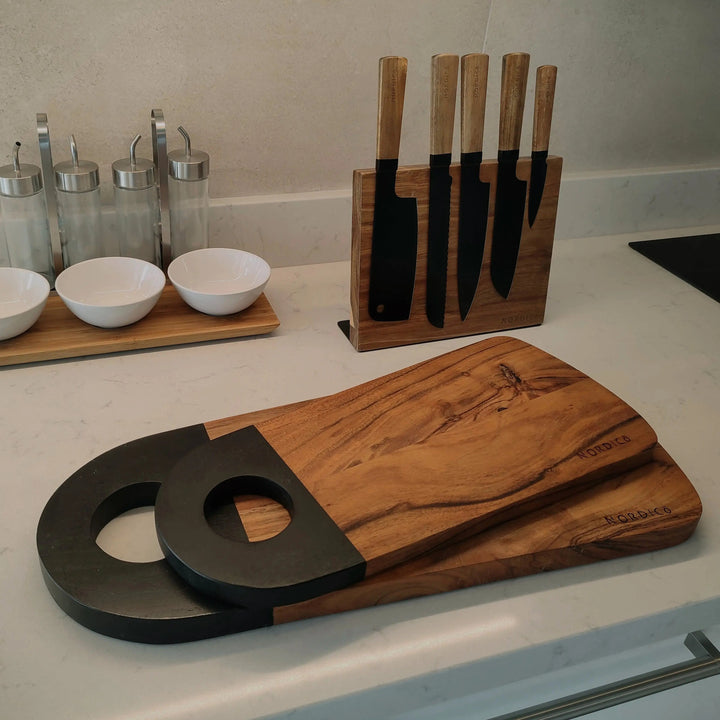 Modern kitchen display featuring Nordico medium and large acacia cutting boards with sleek black handles.